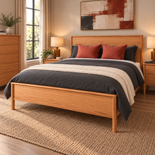 Load image into Gallery viewer, A medium brown wooden bed frame with a slatted headboard and footboard, styled with dark gray and rust red bedding, set in a warm, modern bedroom.