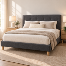 Load image into Gallery viewer, A dark gray upholstered bed frame with a tall tufted headboard and light wood legs, styled with cream bedding, beige pillows, and a textured throw blanket in a bright, modern bedroom.