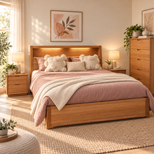 Load image into Gallery viewer, A warm, modern bedroom scene featuring a light oak wood bed frame with a matching headboard and footboard, dressed in dusty pink bedding and textured cream throw pillows and a knit blanket. The room is styled with a matching wooden dresser, nightstands, a woven rug, and soft natural light filtering through the window.