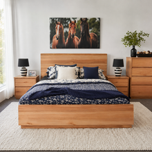 Load image into Gallery viewer, A modern bedroom featuring a light oak wood bed frame with a matching headboard and footboard, styled with navy blue and white patterned bedding. Above the bed is a large rectangular canvas print of three horses.