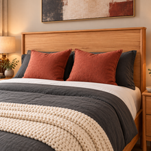 Load image into Gallery viewer, A neatly made bed in a warm, modern bedroom setting, featuring a light wood headboard, dark gray bedding, rust-orange accent pillows, a cream knit throw blanket, and a matching wood nightstand.