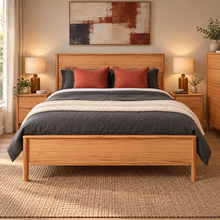 Load image into Gallery viewer, A wooden bed frame with a matching headboard and footboard, styled with dark gray bedding, rust-red pillows, and a textured cream throw blanket, set in a warm, modern bedroom.