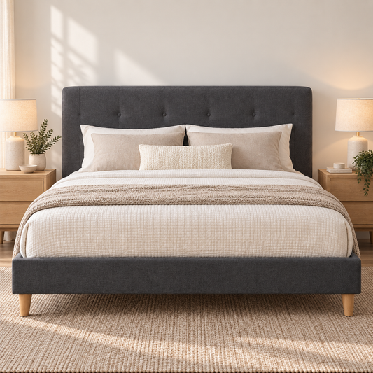 A dark gray upholstered bed frame with a tufted headboard and matching footboard, styled with cream bedding, beige pillows, and a textured throw blanket in a bright, modern bedroom.