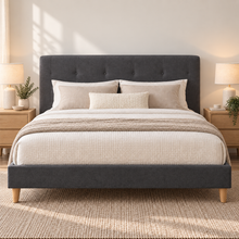 Load image into Gallery viewer, A dark gray upholstered bed frame with a tufted headboard and matching footboard, styled with cream bedding, beige pillows, and a textured throw blanket in a bright, modern bedroom.