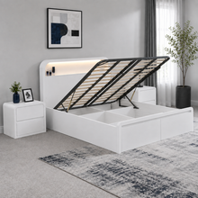 Load image into Gallery viewer, A modern white storage bed with its headboard raised to show the slatted frame, set in a styled bedroom with a matching nightstand, gray rug, and wall art.