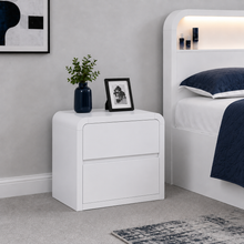 Load image into Gallery viewer, A modern white two-drawer nightstand in a bedroom setting, styled with a dark blue vase of greenery and a black picture frame, next to a white bed with navy bedding.