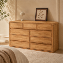Load image into Gallery viewer, An oak dresser with 9 drawers, rounded corners and seamless handles. Set in a warm bedroom complimented with neutral colours. The dresser has three smaller drawers on the top, with 6 bigger drawers at the bottom in a 2x3 pattern.