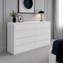 Load image into Gallery viewer, A modern white wooden dresser with ten drawers, styled in a bedroom setting with a black table lamp, a small potted plant, and framed wall art.