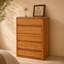 Load image into Gallery viewer, A oak tallboy with 5 long drawers in a bedroom setting with neutral colours and leaves coming out from the side. 