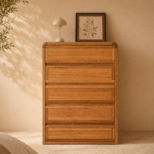 Load image into Gallery viewer, A oak tallboy with 5 long drawers in a bedroom setting with neutral colours and leaves coming out from the side. 