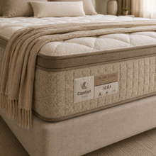 Load image into Gallery viewer, A close-up of a Comfort Sleep Aura mattress in a beige tufted frame, styled with a matching beige throw blanket and pillows in a softly lit bedroom.